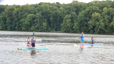 People standing and kneeling while on paddle boards in a lake