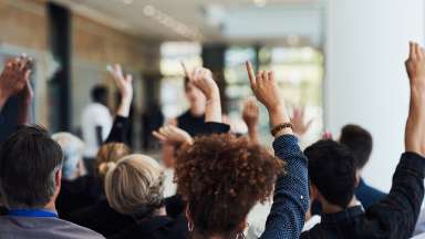 People in a meeting with their hands raised to ask a question