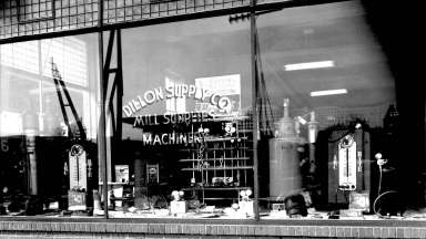 A black and white photograph of the window of a storefront that reads Dillion Supply Co. Mill Supples Machinery