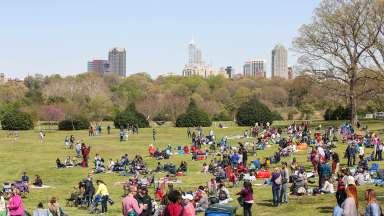 Event at Dix Park with Raleigh skyline in the background and lots of people out on a green lawn