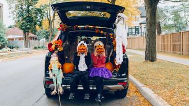 children with pumpkins sitting on a car trunk
