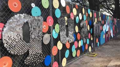 a construction fence is decorated with brightly painted records and shiny objects