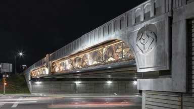 An overpass lit up at night trimmed with intricate metal work by Vicki Scuri