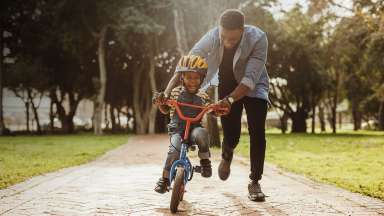 Man helping boy balance on a bike down a path in a park