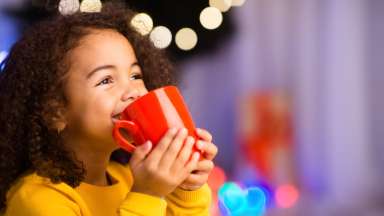 a little girl smiling while sipping out of a red mug