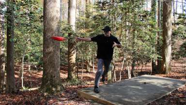 man throwing a disc on a wooded disc golf course