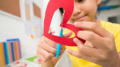 a little girl cutting out a heart with red paper