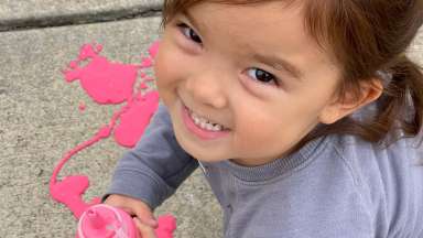 a little girl posing for a picture playing with pink paint on the concrete