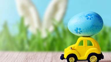 yellow car with blue egg on top and bunny ears in the back