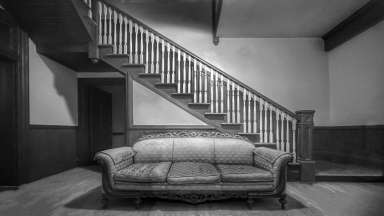 black and white image of a room with a couch and stairs