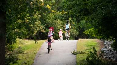 children riding bikes on paved trail with helmets on