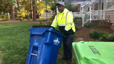 Solid Waste Services employee rolls cart from a backyard