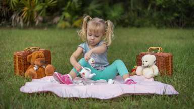 an image of a little girl having a tea party picnic with her stuffed teddy bears on the grass
