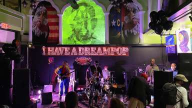 A band plays on a stage with American and North Carolina imagery in the background