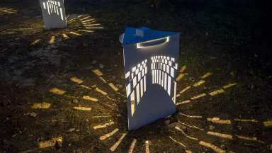 Light streams out of a white box with cut outs casting shadows on the ground