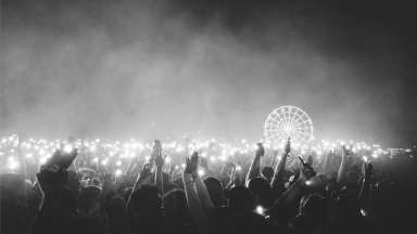 Crowd with hands raised enjoying Dreamville Festival at night with ferris wheel in background