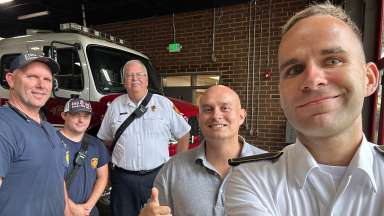 Sven posing with other firefighters in front of a fire truck parking in garage