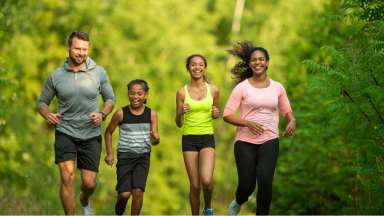 Four people running on the a trail with fall leaves on the trees.
