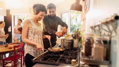A couple is cooking a pan of food at a gas stovetop