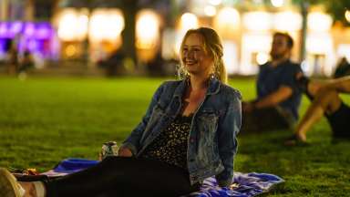 a person sitting on a lawn smiling while watching a movie