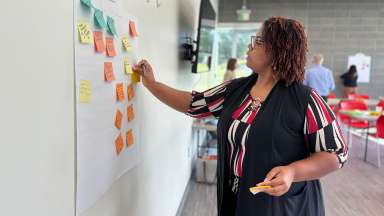 At a feedback session, person adds ideas by pasting post-it notes to the wall under a category.