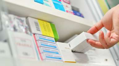 a hand reaching to grab a prescription from pharmacy shelf