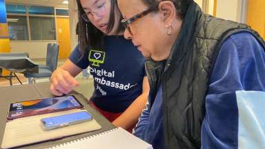 Volunteer and woman sit at table looking at iPhone device.