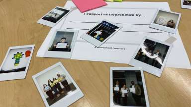 Photographs of winners are laid out on a table with a sheet of paper than says &quot;I support entrepreneurs by&quot;