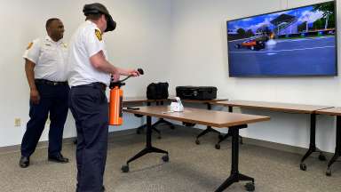 Person with VR headset holds a extinguisher tool while another person looks at the screen