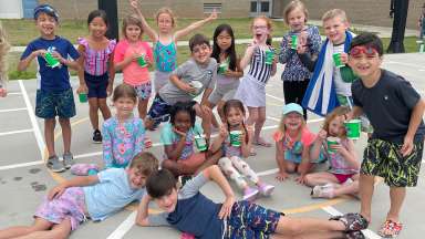 an image of kids posing outside for a picture in summer clothes and bathing suits holding snow cones.