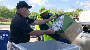 Two men drop documents to be shredded in a large bin