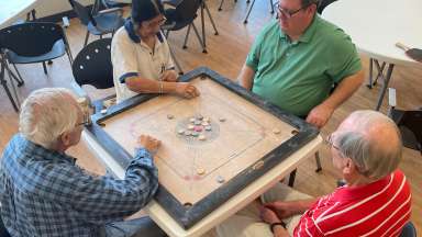 4 people sitting a square table playing carrom