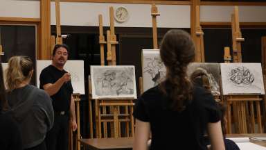 Instructor standing at an easel holding a drawing with students looking on