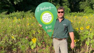 man holding where I belong sign standing in a field of sunflowers