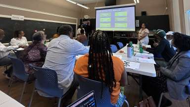 Photo of working group sitting at tables looking at presentation slide and speaker