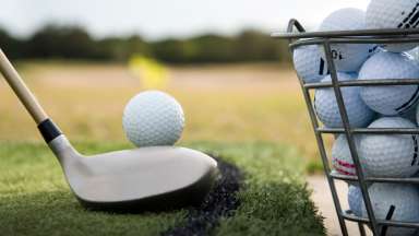 a golf club and a basket of golf balls sitting on the grass