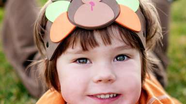 Kid outside with a turkey hat on. He is posed smiling at the camera.