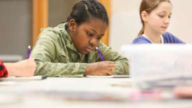Young Black teen working hard on a drawing at a table in an art studio.