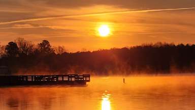 the sun rising over a lake with dock