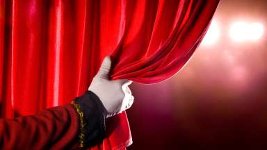 a red curtain being pulled open by a white gloved hand