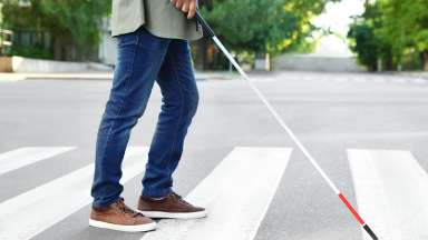 Person walking on crosswalk, led by white cane