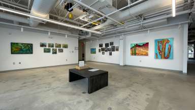 Gallery with several artists work displaying including colorful paintings and framed works on paper