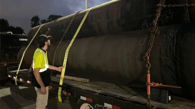 Pipes loaded onto a flat bed truck with a Raleigh Water employee standing next to the load.