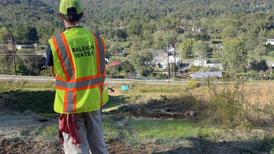 Raleigh Water employee standing in front of mountains in Western North Carolina, wearing a safety vest.