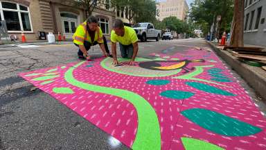 Two people installing a brightly colored mural on a Raleigh street