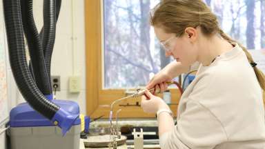 Young woman with blond hair wearing safety googles working with a torch to make jewelry