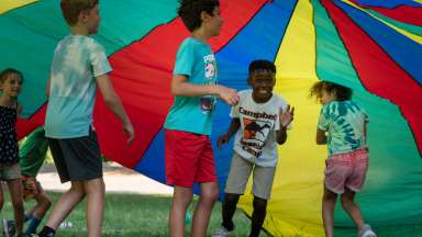 children playing with a colorful parachute at summer camp