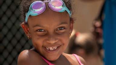 a smiling child with swimming goggles on the top of their head