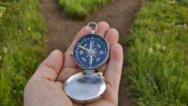 a hand holding a compass with a forked path ahead