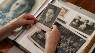 Close-up of elderly person’s hands holding black-and-white photographs from vintage photo album